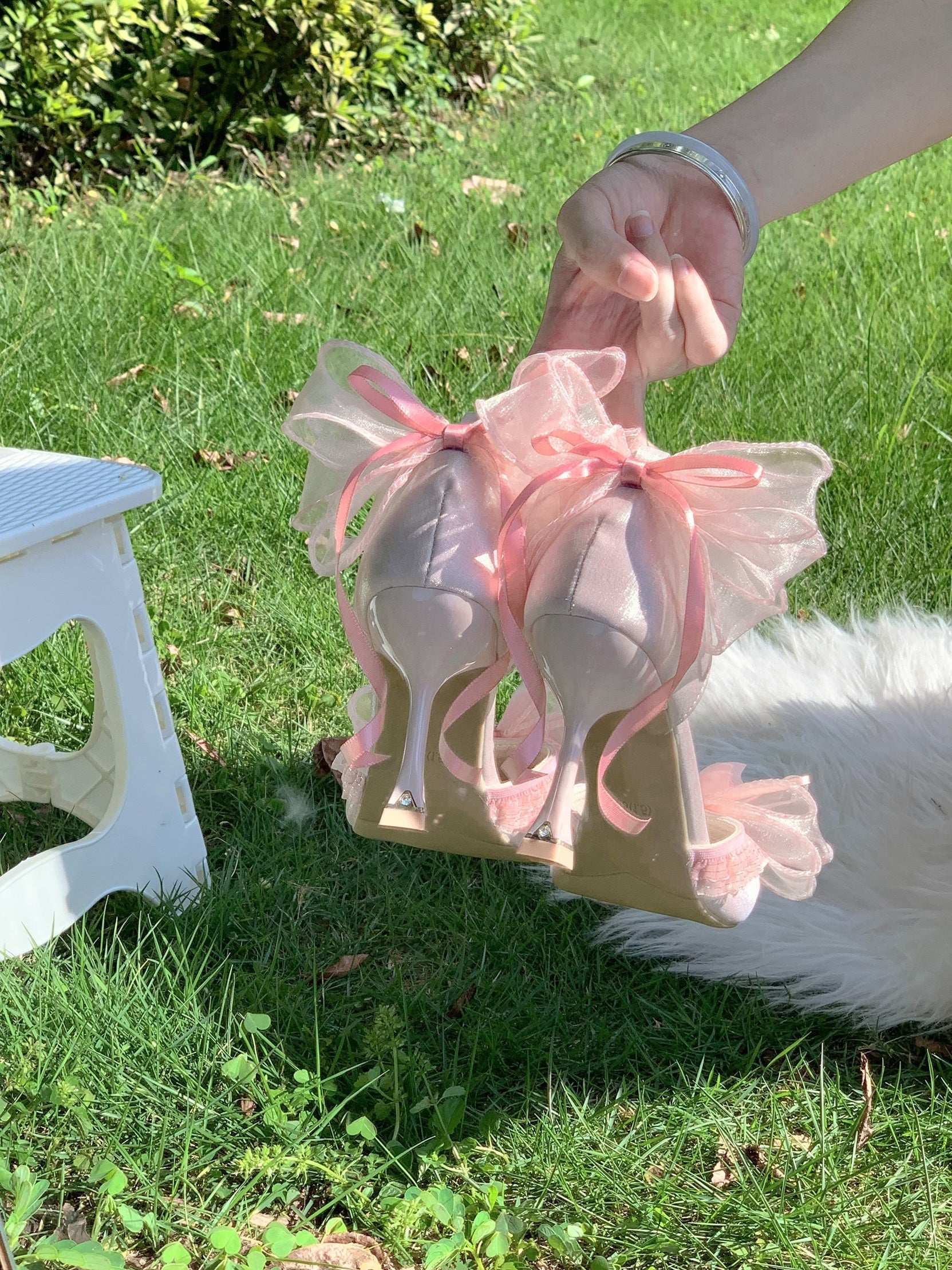 Pink high-heeled shoes with pink ribbons held by a hand on a grassy background