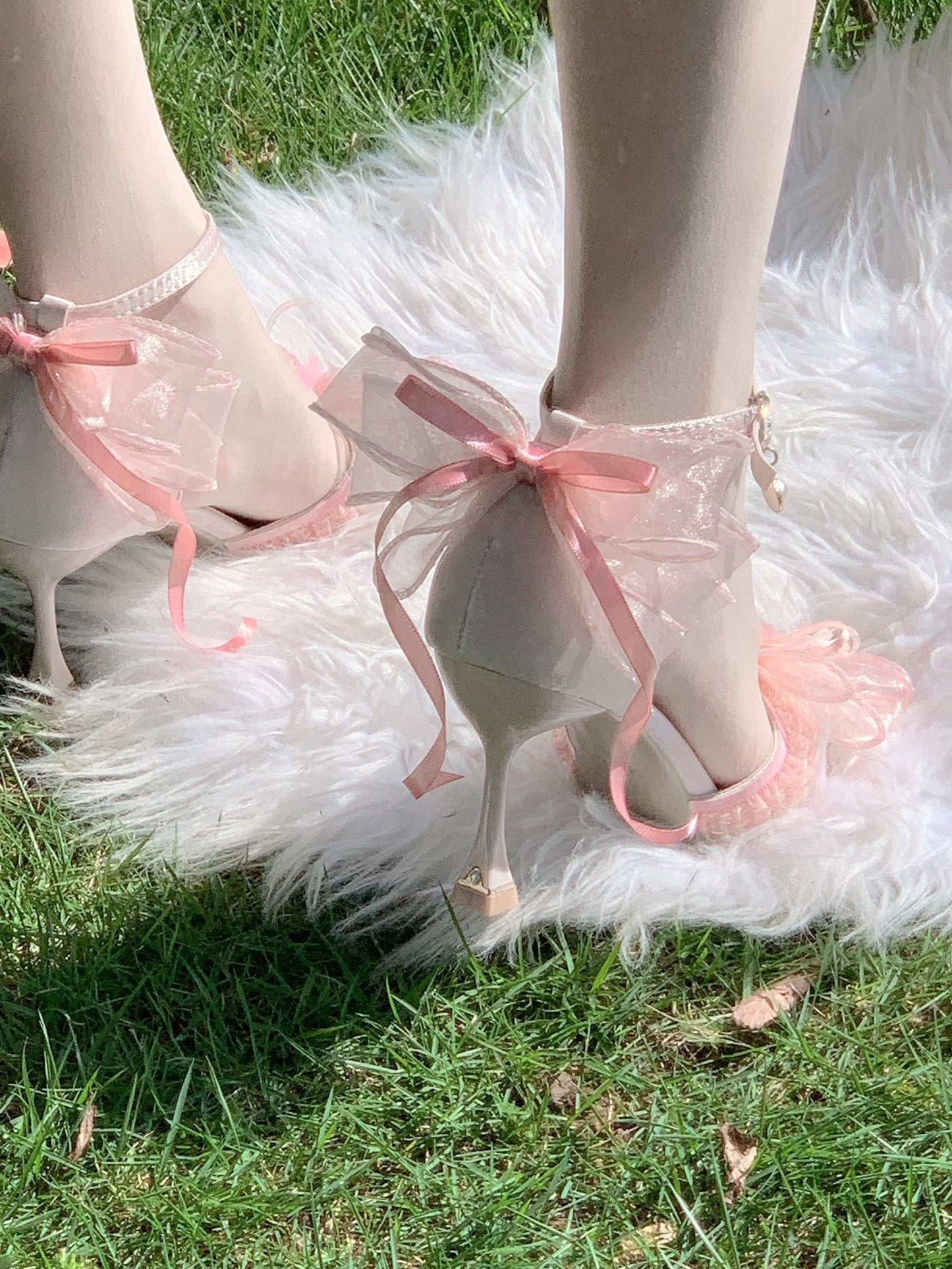 Pink high-heeled shoes with pink ribbons on a grassy background