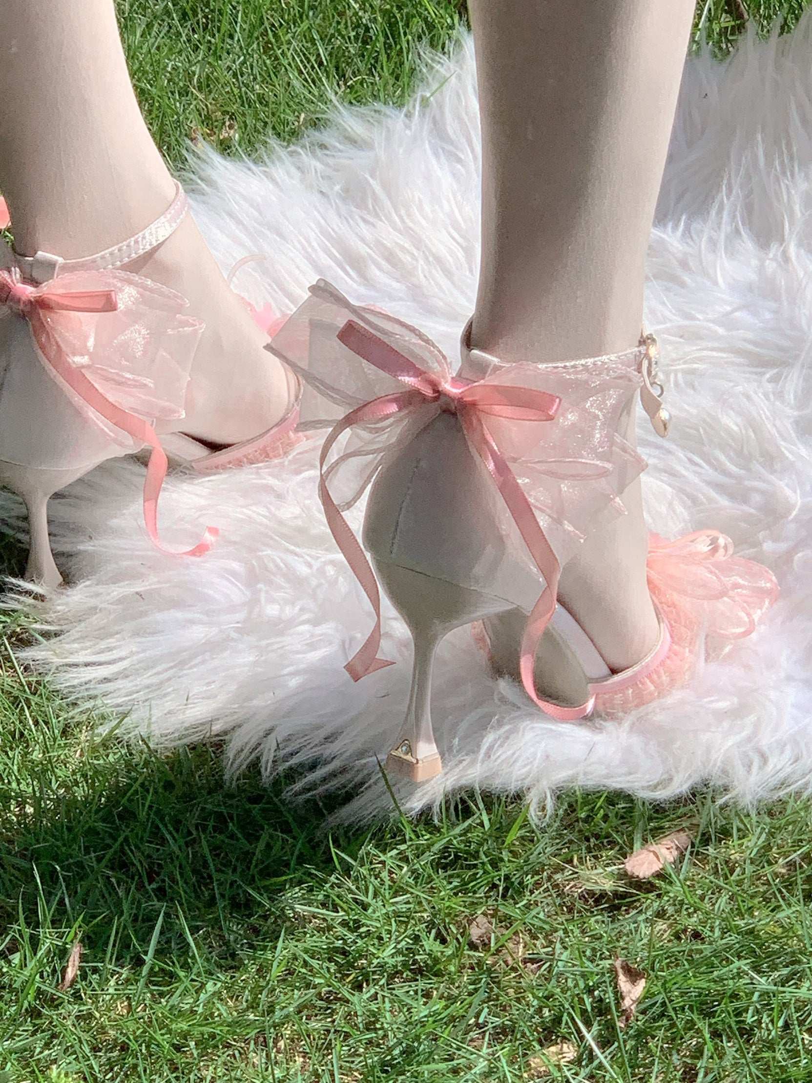 Pink high-heeled shoes with pink ribbons on a grassy background