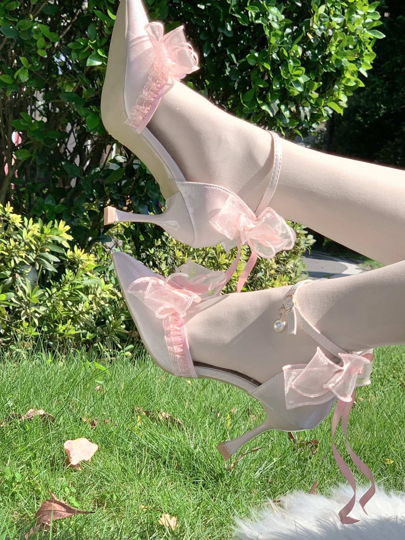 Pink high-heeled shoes with pink bows on grass and green foliage background
