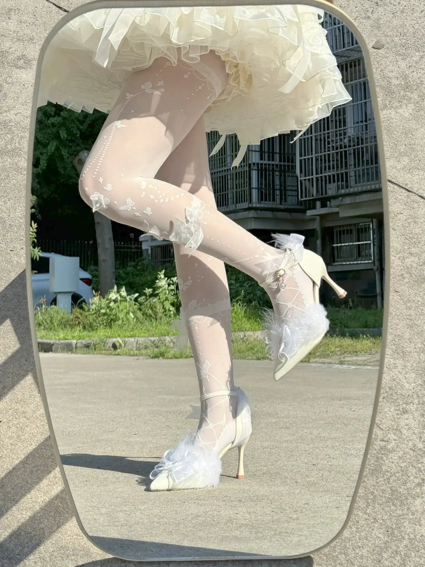 White floral high-heeled shoes worn with sheer stockings on a reflective surface.