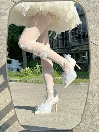 White floral high-heeled shoes worn with sheer stockings on a reflective surface.
