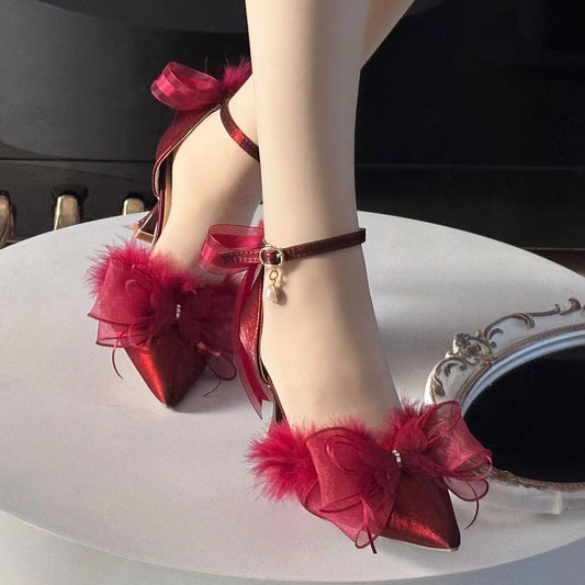 Red high-heeled shoes with fluffy details on a white surface.
