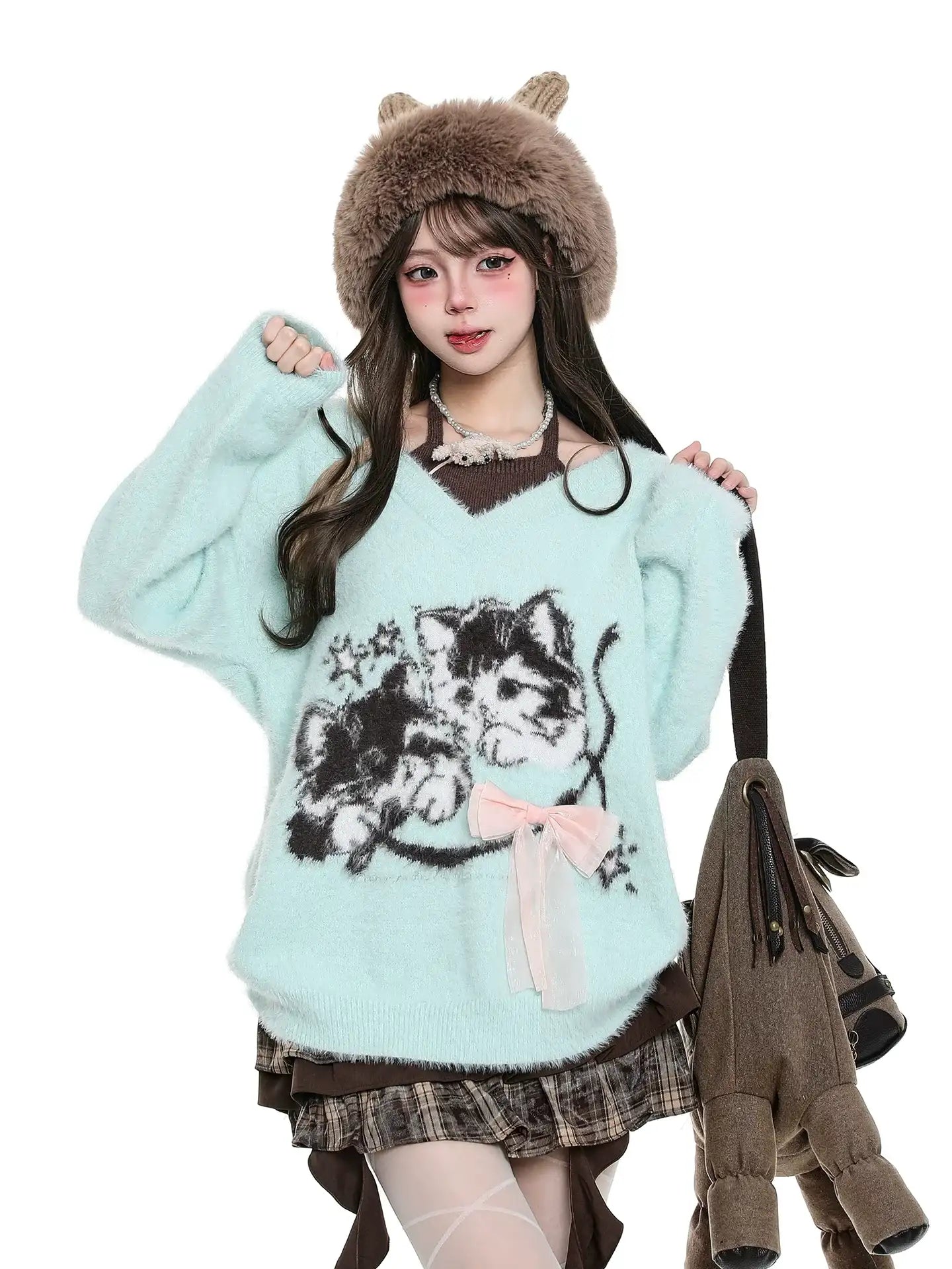 Woman wearing a light blue sweater with a cat design, brown hat, and plaid skirt on a white background.