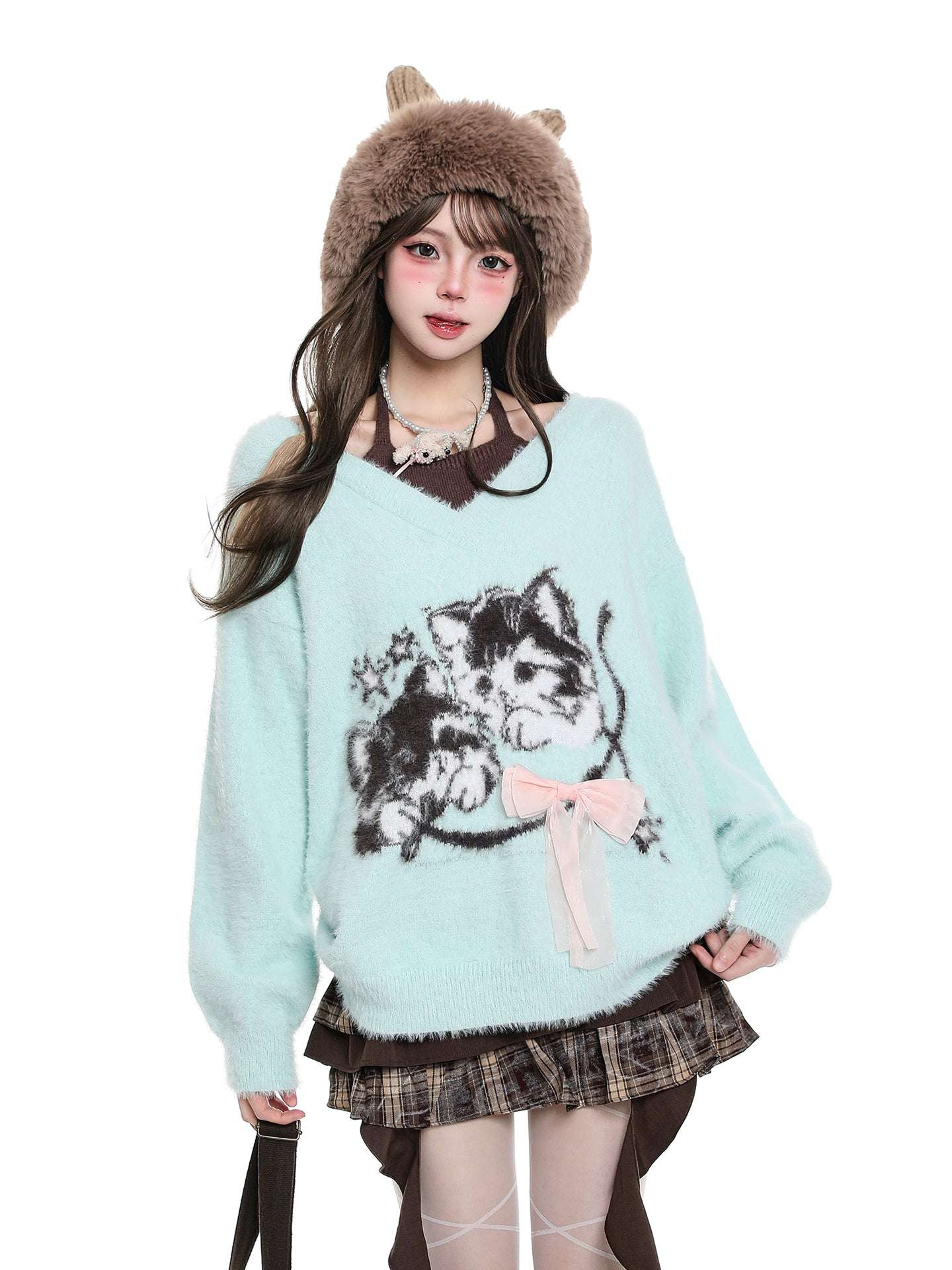 Person wearing a light blue sweater with cat design and a brown hat on a white background