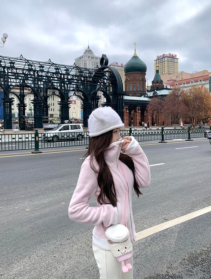 Person in pink coat and white hat standing on a street with architectural buildings in the background