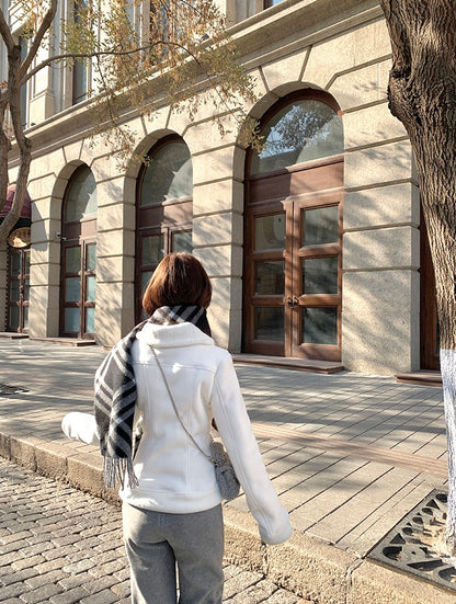 Person walking on a sidewalk in front of a building with arched windows and wooden doors.