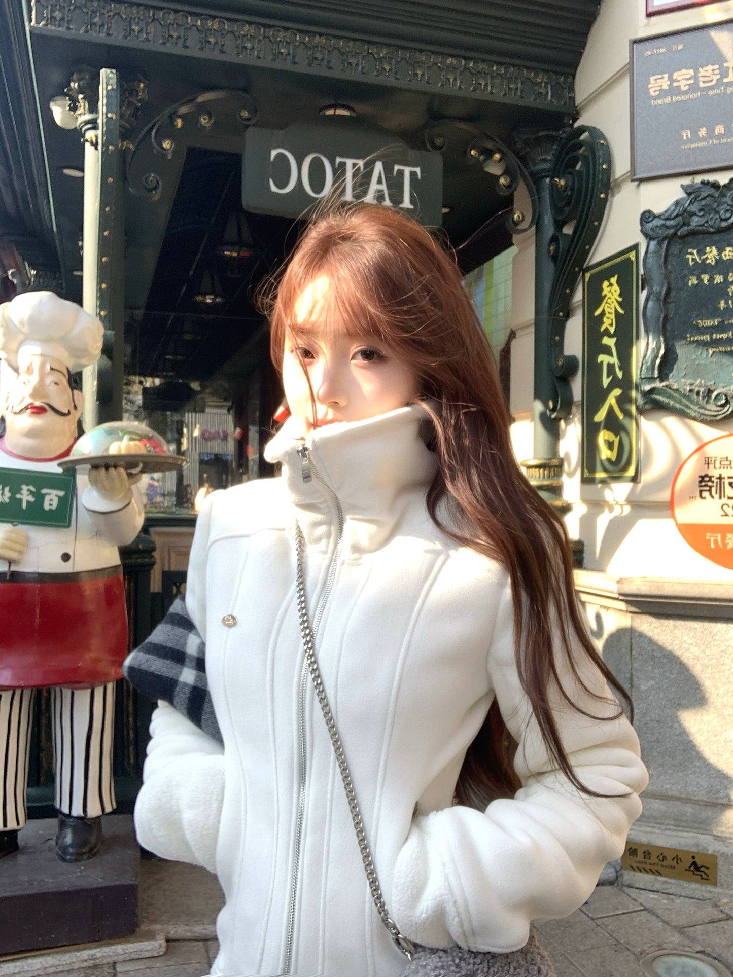 Woman in a white coat standing in front of a building entrance with decorative elements.