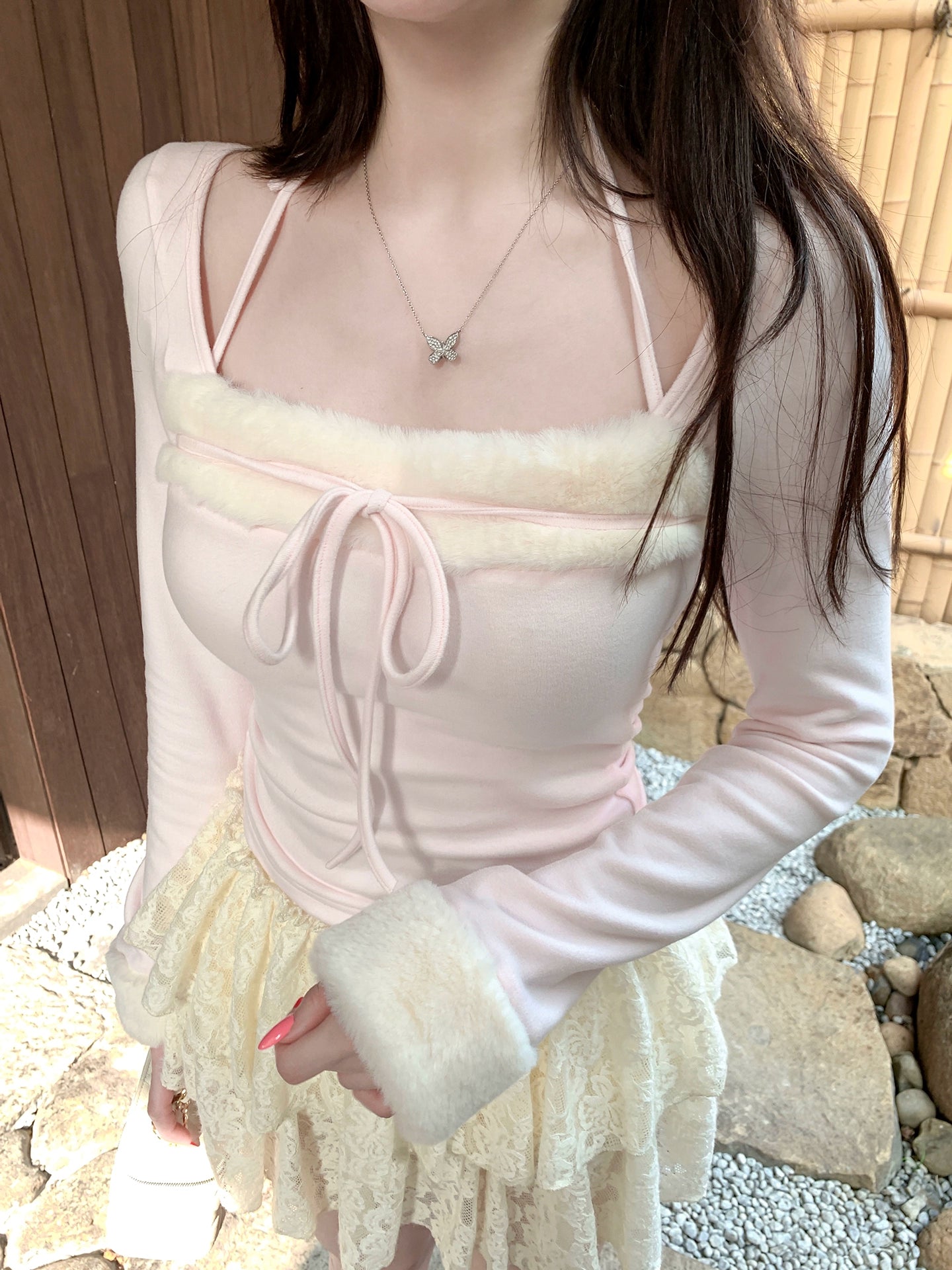 Person wearing a light pink long-sleeve top with sheer panels and white fur cuffs, standing outdoors.