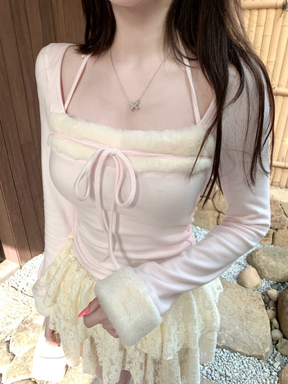 Person wearing a light pink long-sleeve top with sheer panels and white fur cuffs, standing outdoors.