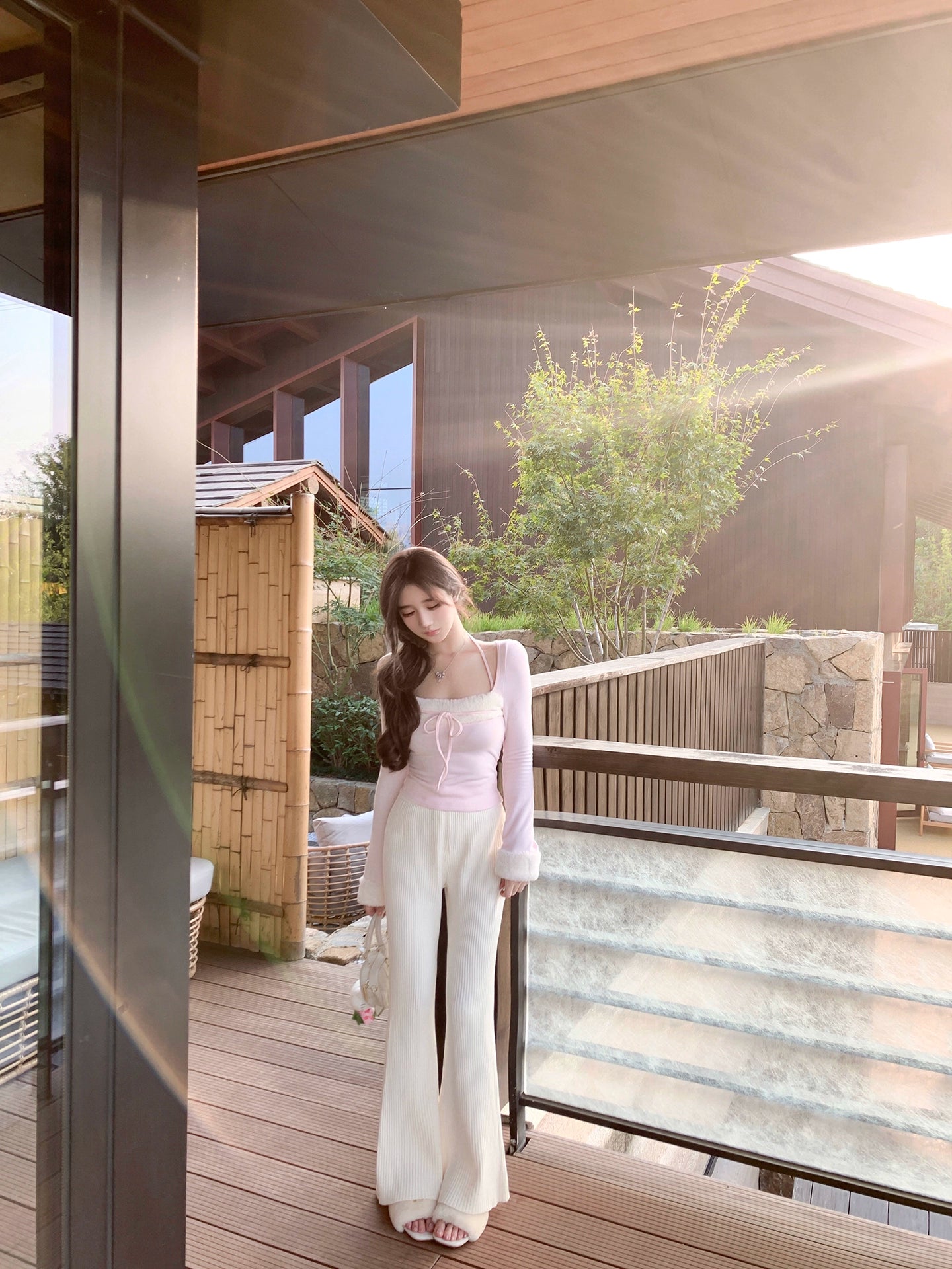 Woman in a white outfit standing on a wooden deck with a modern building and greenery in the background