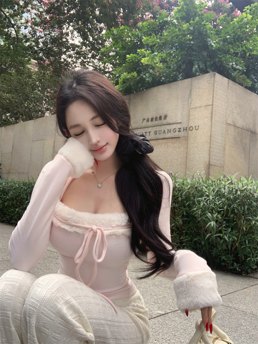 Woman in a light pink outfit sitting outdoors with greenery and a stone wall in the background