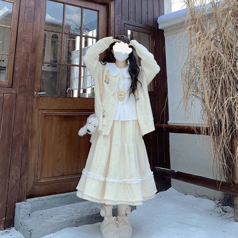 Person in a cream-colored outfit standing in front of a wooden door.