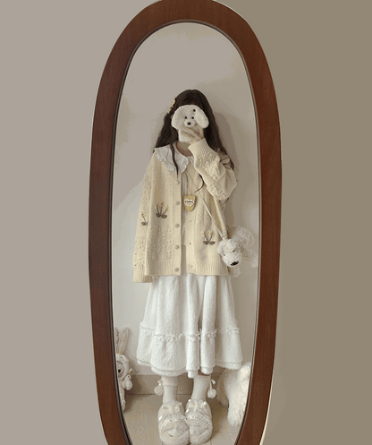 Person wearing a cream-colored cardigan with floral patterns in front of an oval mirror.