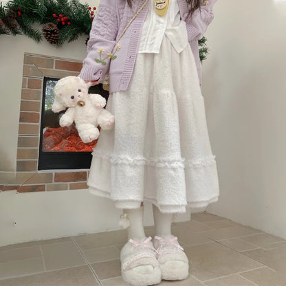 Person wearing a light purple cardigan, white lace skirt, and white shoes holding a white teddy bear in front of a fireplace.