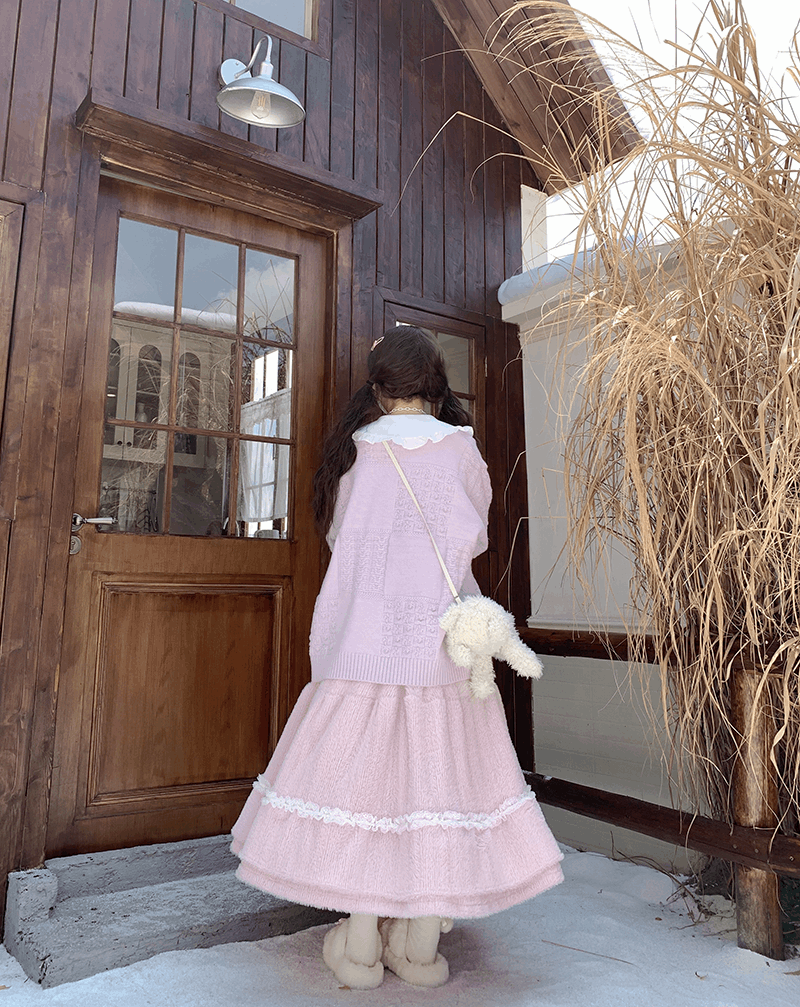Person in a pink dress standing in front of a wooden door with snow on the ground.