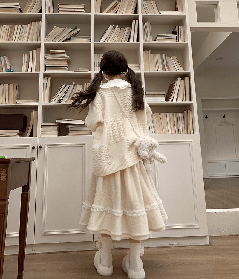 Person in a white outfit standing in front of a bookshelf filled with books.