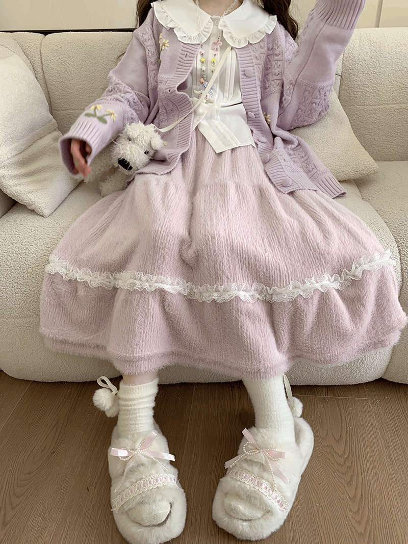 Woman wearing a pink outfit with a white collar and white shoes, sitting on a beige couch.