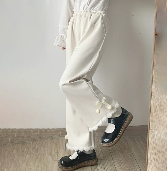 Person wearing white pants with pom-pom details and black shoes on a wooden floor.