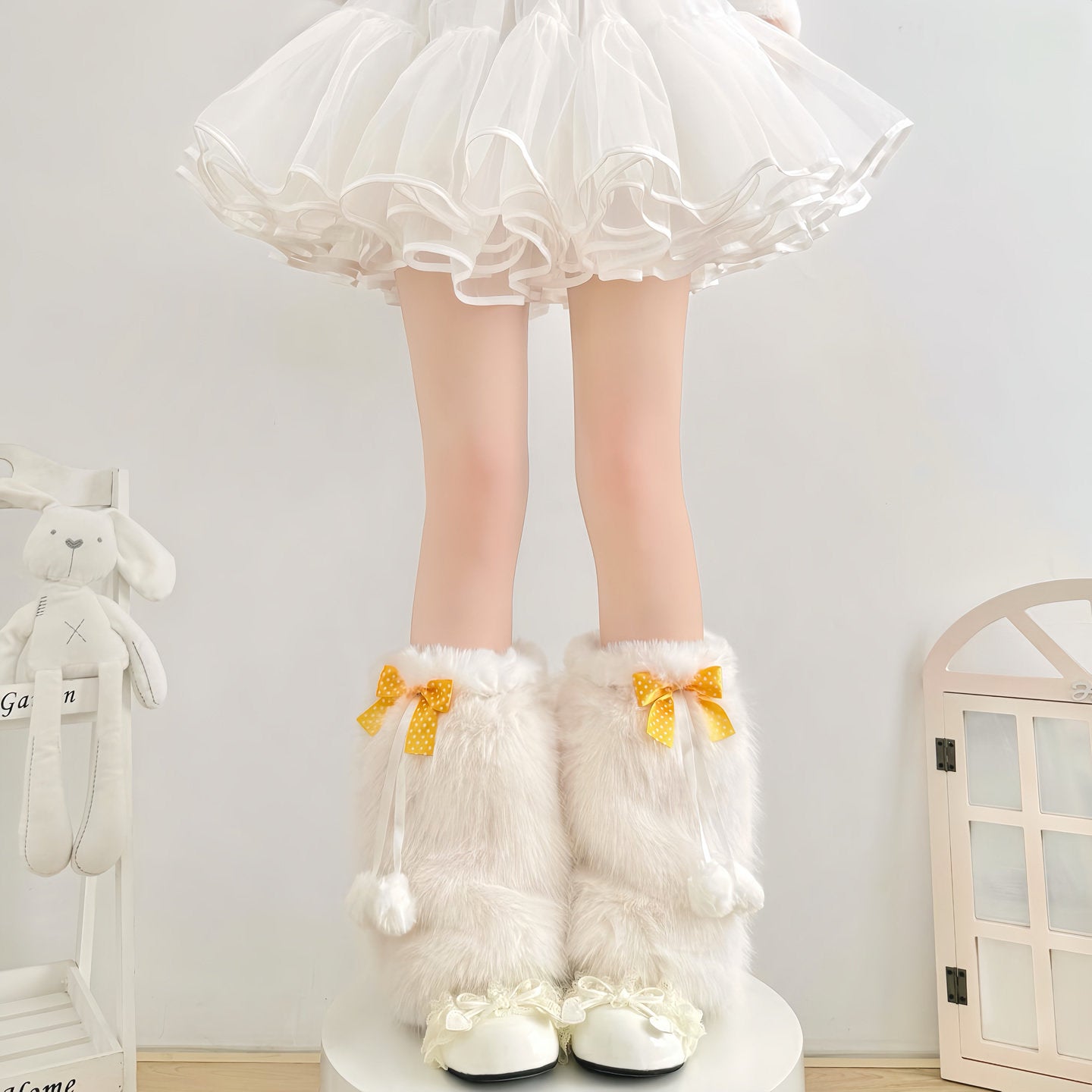 White fluffy knee-high boots with yellow bows worn by a person in a white skirt.