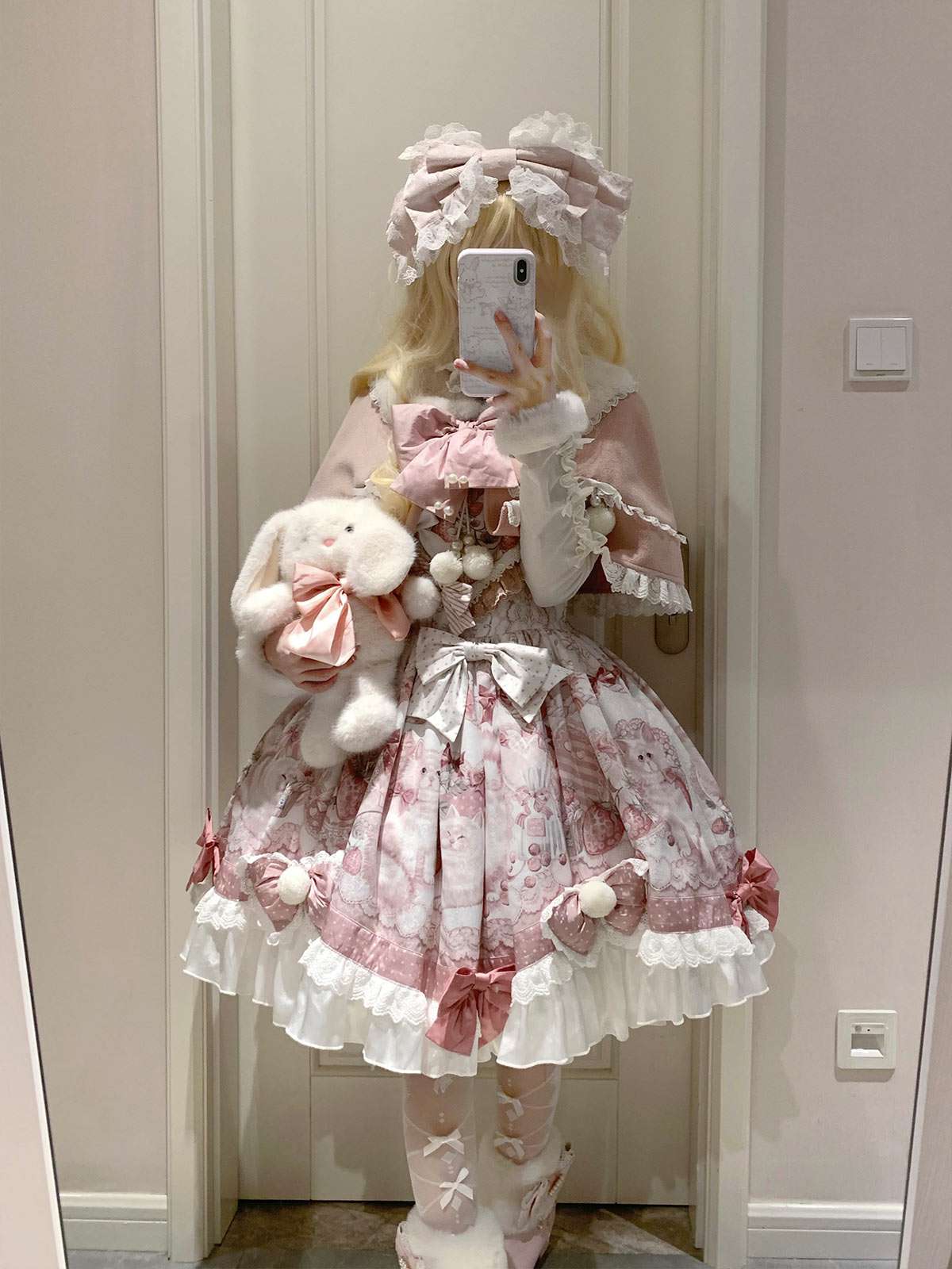 Person wearing a pink and white Lolita outfit with a teddy bear, standing in a room.