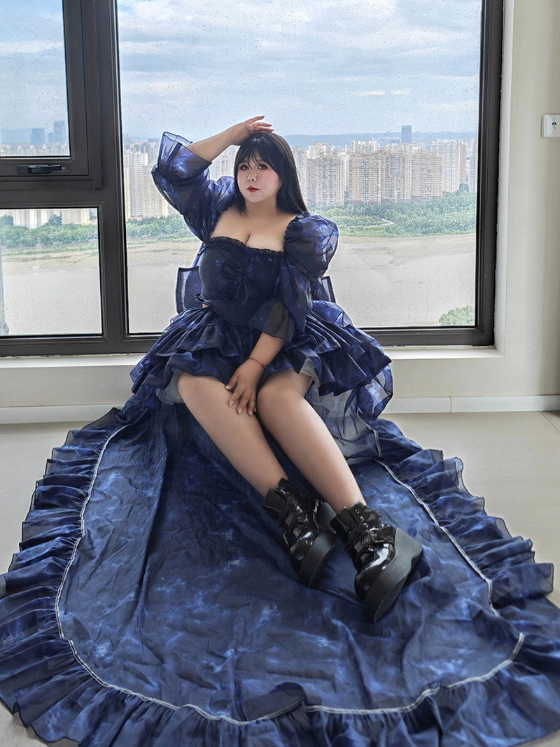 Plus Size Woman in a blue dress sitting by a large window with a cityscape view.