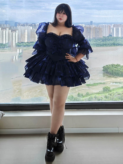 Plus Size Woman wearing a dark blue ruffled dress with black boots standing in front of a large window with a cityscape view.