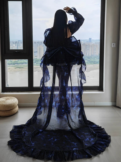 Person wearing a long, dark blue and white dress standing in front of a large window with a cityscape view.