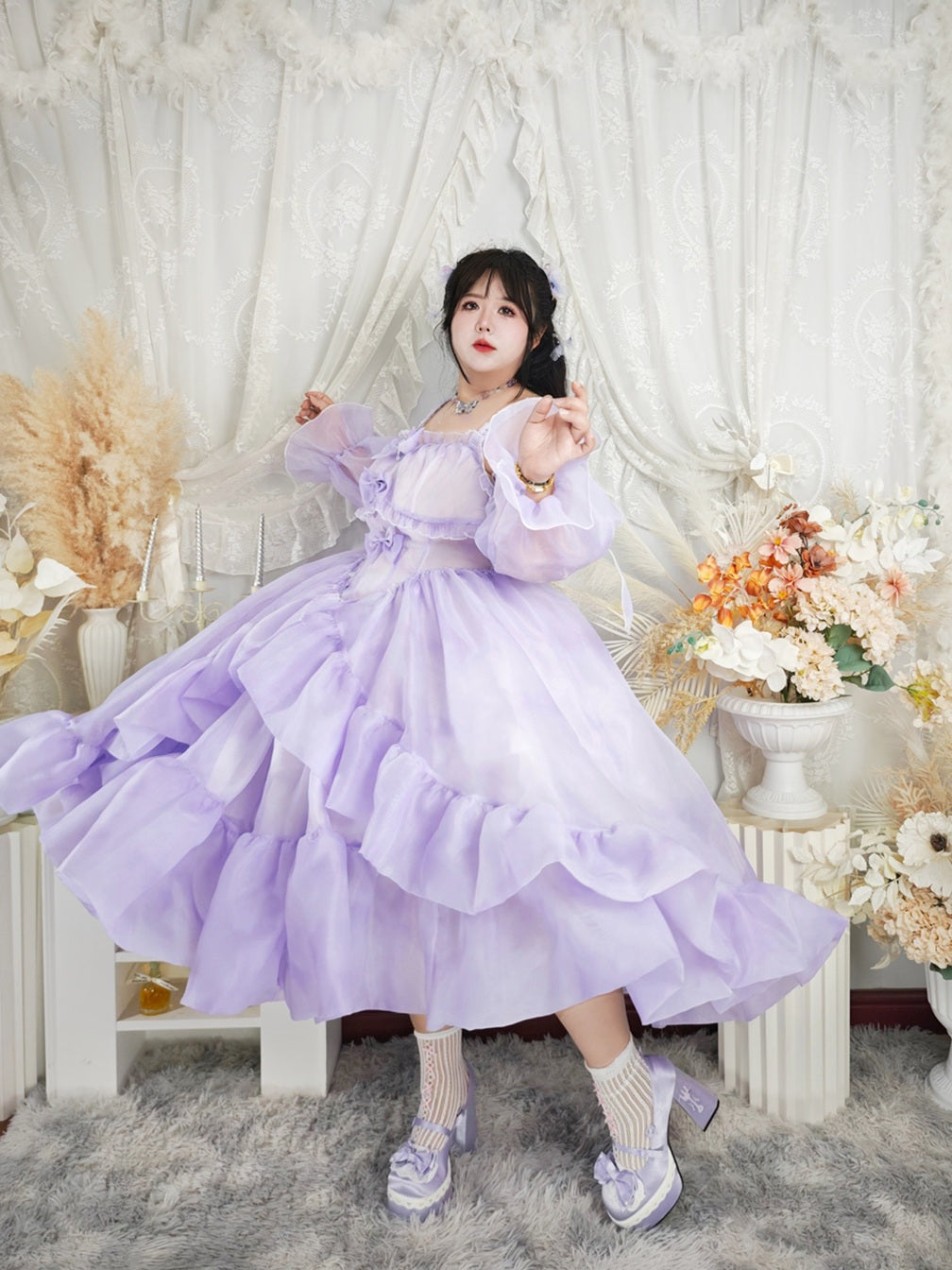Person wearing a purple dress in a decorated room with flowers and white curtains.