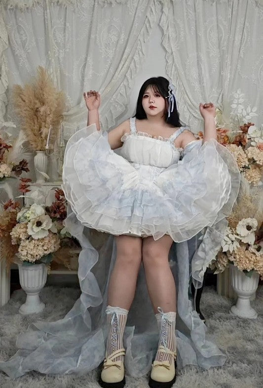 Woman in a white dress with sheer overlay in a decorated room with flowers and curtains.