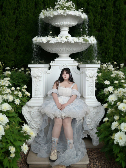 Woman in a white dress sitting on a white fountain surrounded by flowers