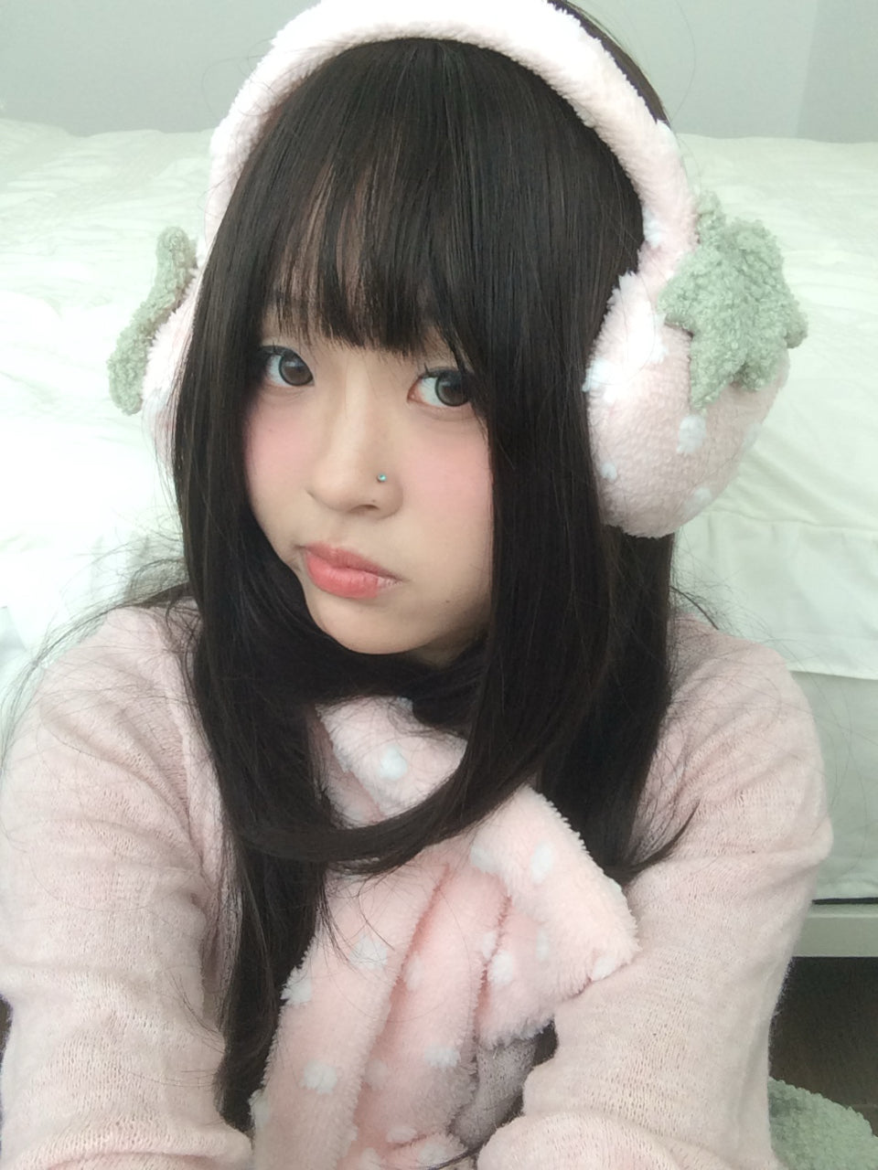 Person wearing pink strawberry earmuffs, sitting on a light-colored couch.