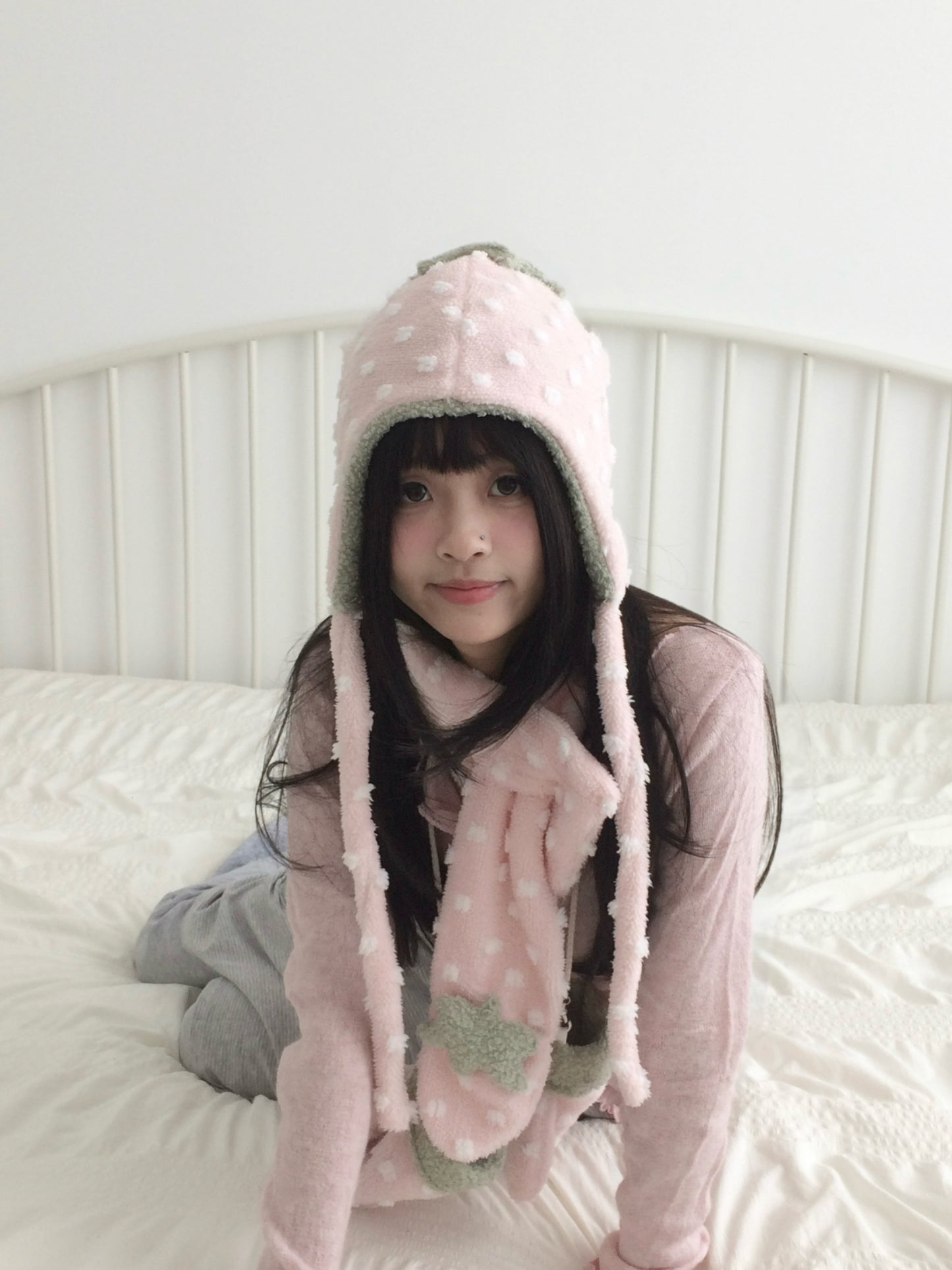 Person wearing a pink strawberry hats with long sleeves on a white bed.