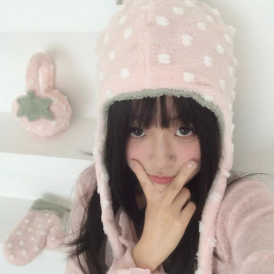 Person wearing a pink polka dot hooded strawberry winter hats with matching gloves on a light background