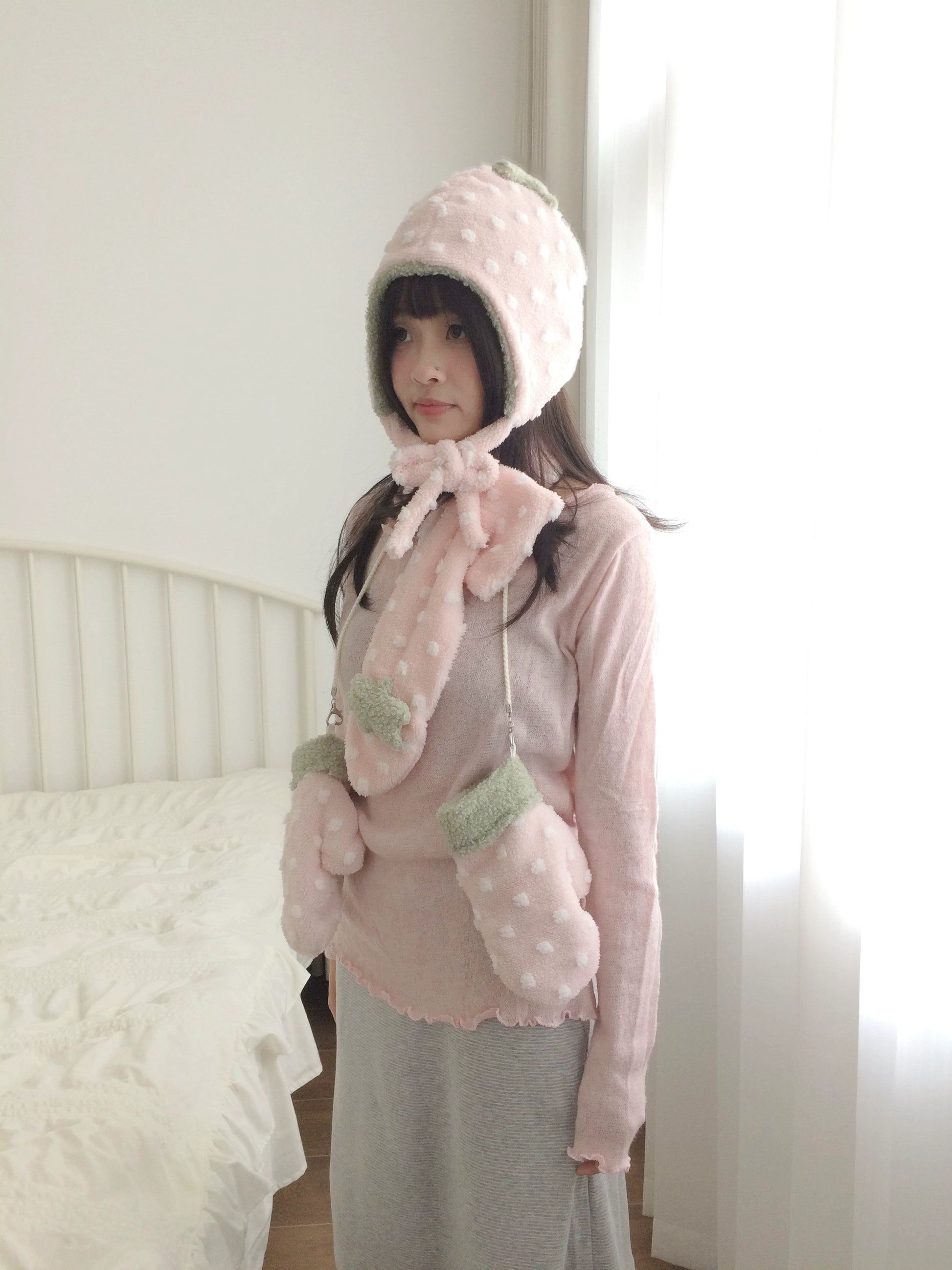 Person wearing a pink strawberry costume with a hood and ears indoors.