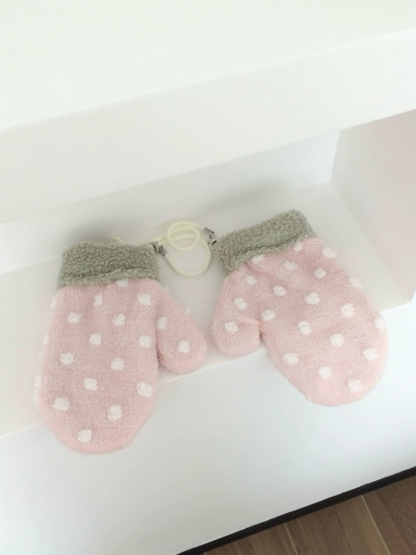 Pair of pink strawberry mittens with white polka dots on a light background