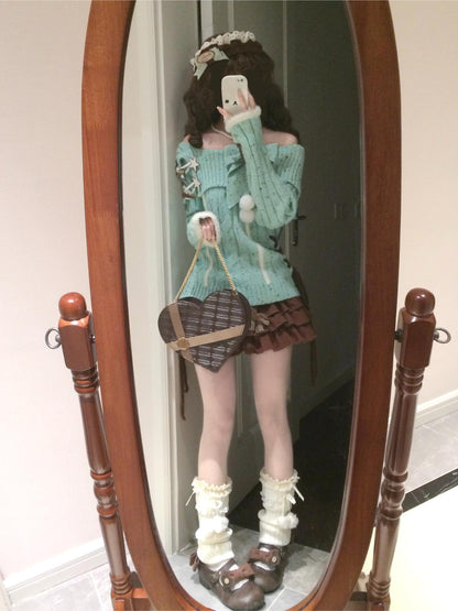 Person wearing a green sweater and skirt, holding a heart-shaped bag, standing in front of a wooden-framed mirror.