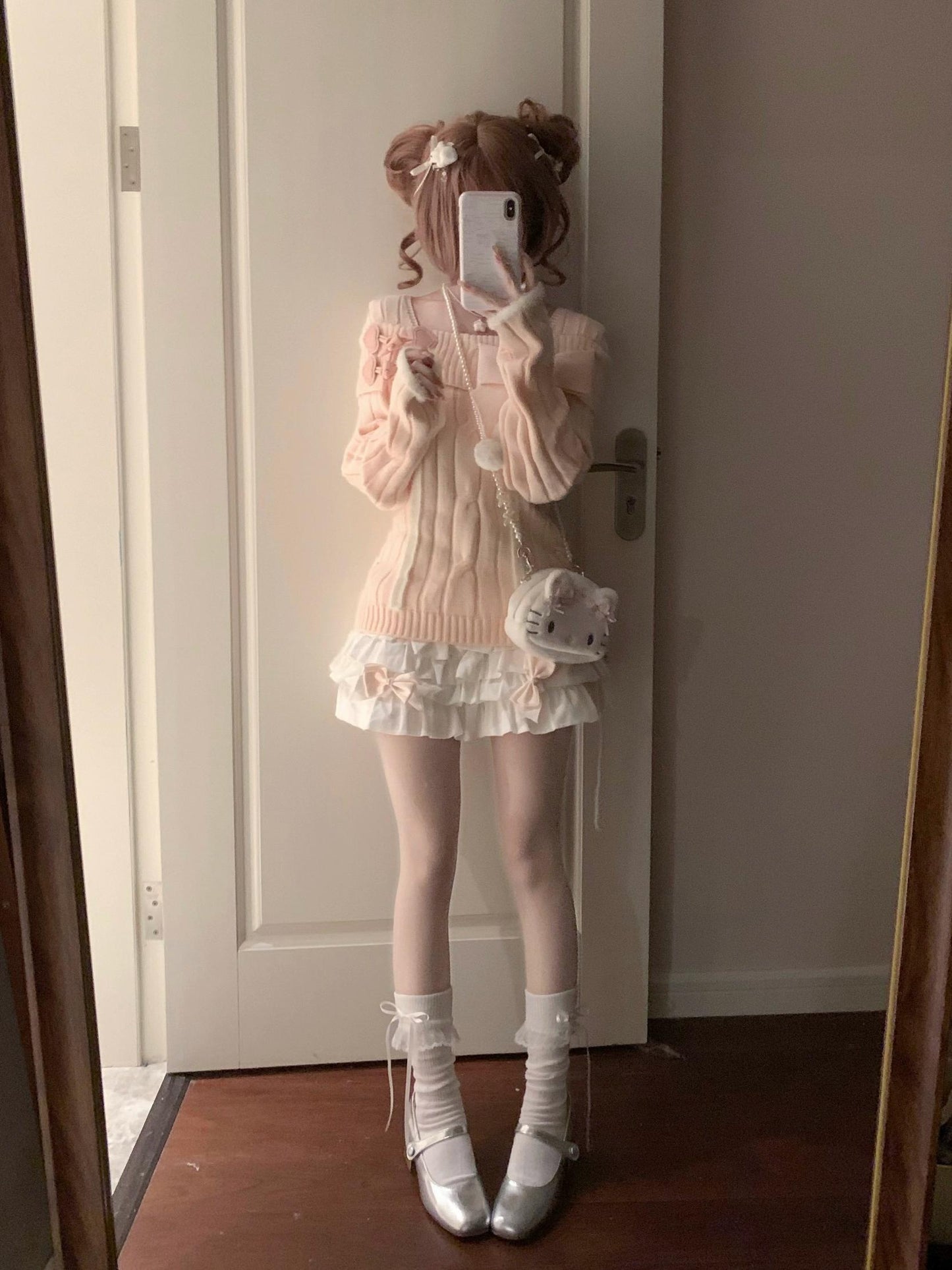 Person taking a mirror selfie wearing a pastel outfit with a white door in the background.