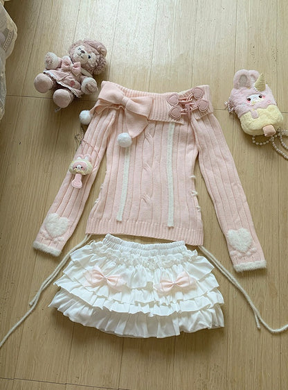 Pink sweater with white ruffled skirt and decorative elements on a wooden floor.