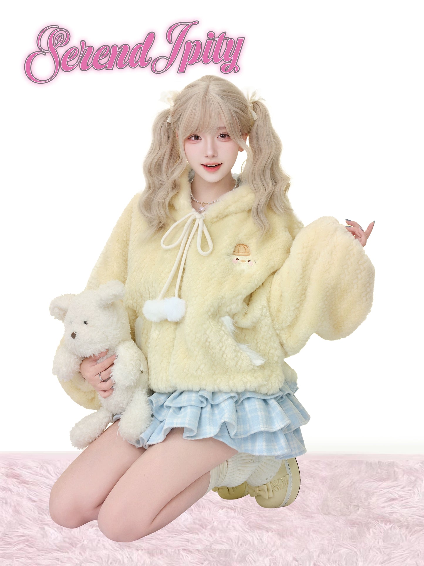Person wearing a fluffy yellow outfit with a teddy bear on a pink background, featuring the brand 'Serendipity'.