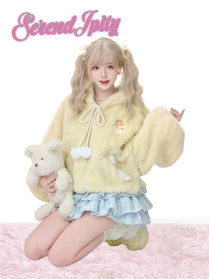 Person wearing a fluffy yellow outfit with a teddy bear on a pink background, featuring the brand 'Serendipity'.