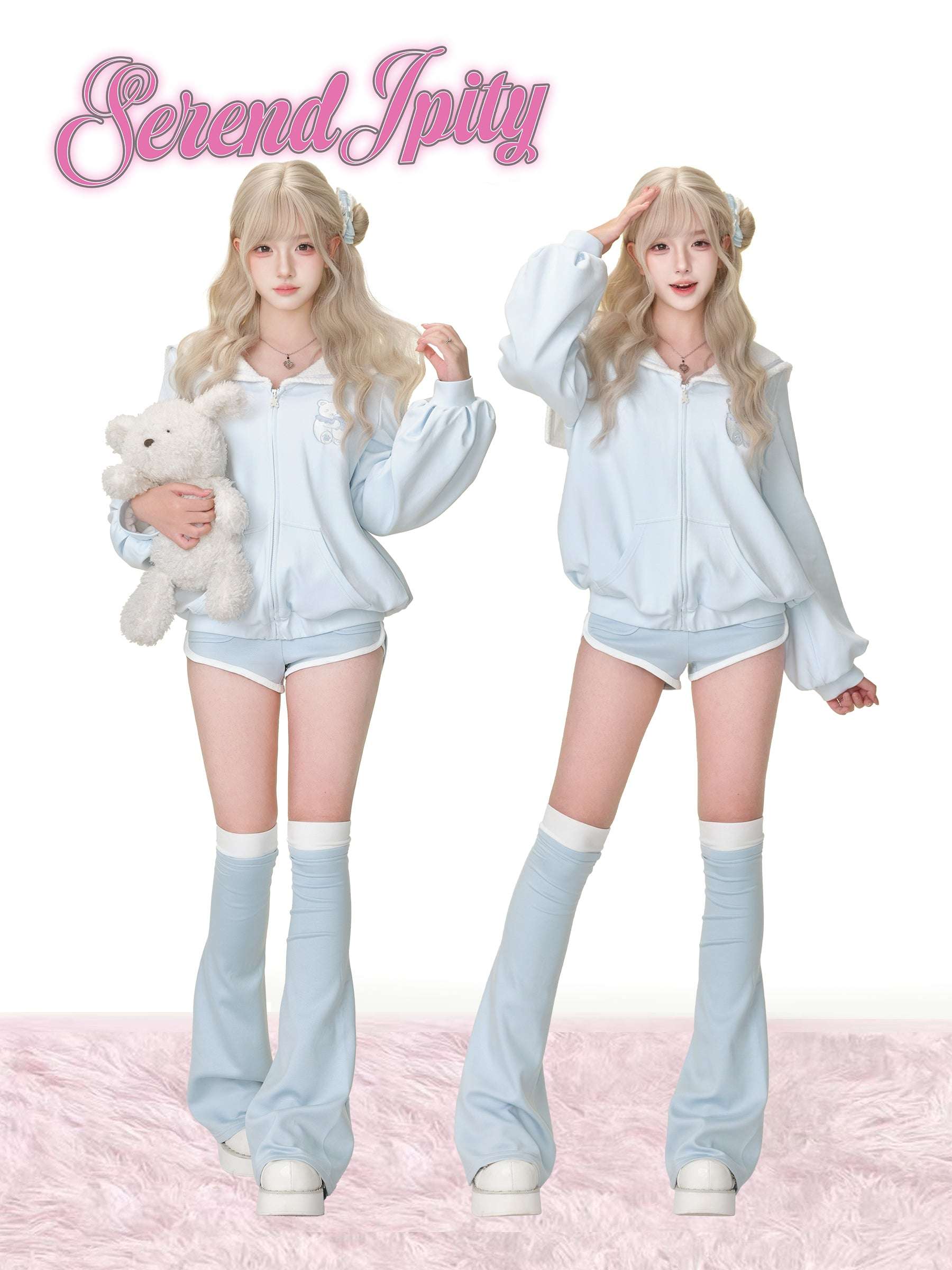 Two people wearing matching light blue outfits with fluffy socks on a pink background, holding a teddy bear.