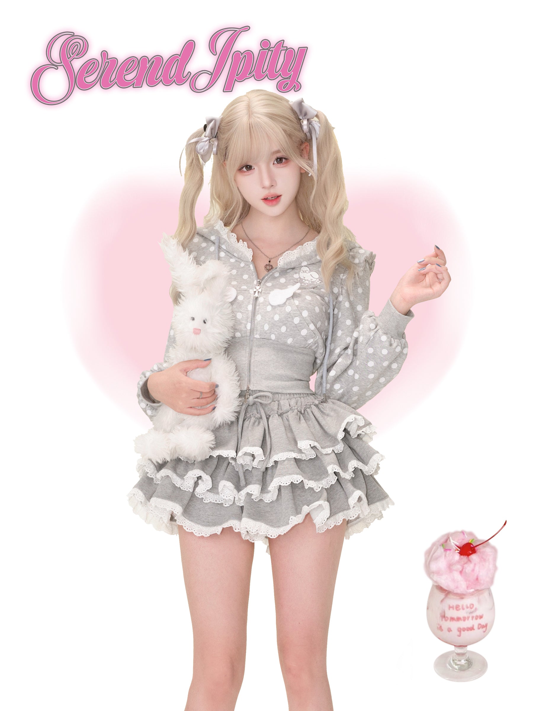 Person wearing a gray polka dot outfit with a fluffy white toy, holding a pink drink with a cherry on top, against a pink background with 'Serendipity' text.