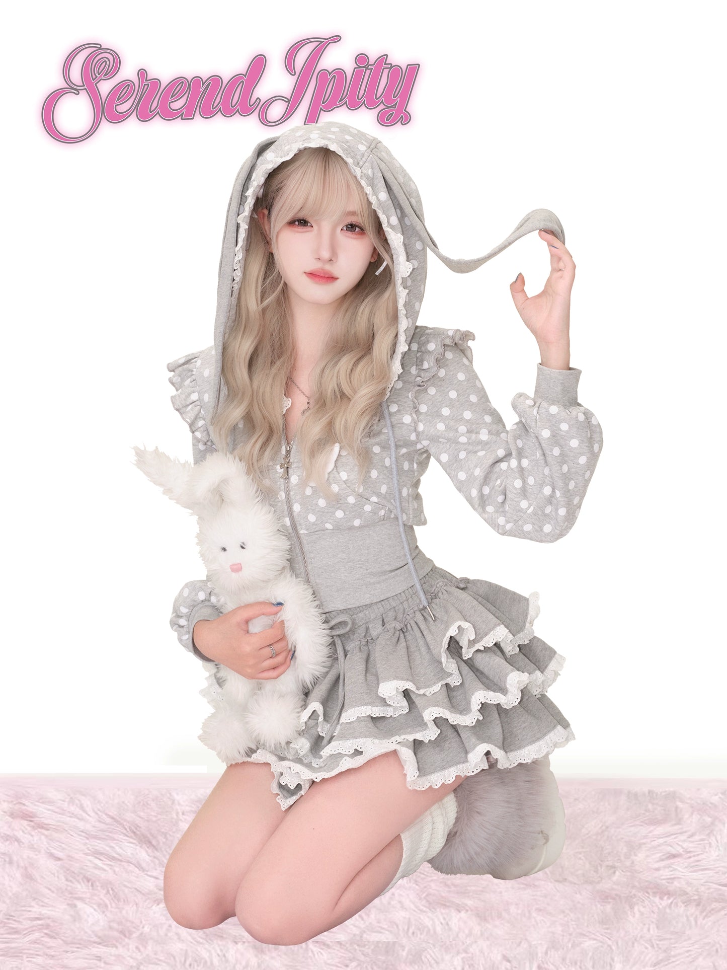 Person wearing a gray polka dot outfit with a hood, holding a plush toy, on a white background with 'Serendipity' text.