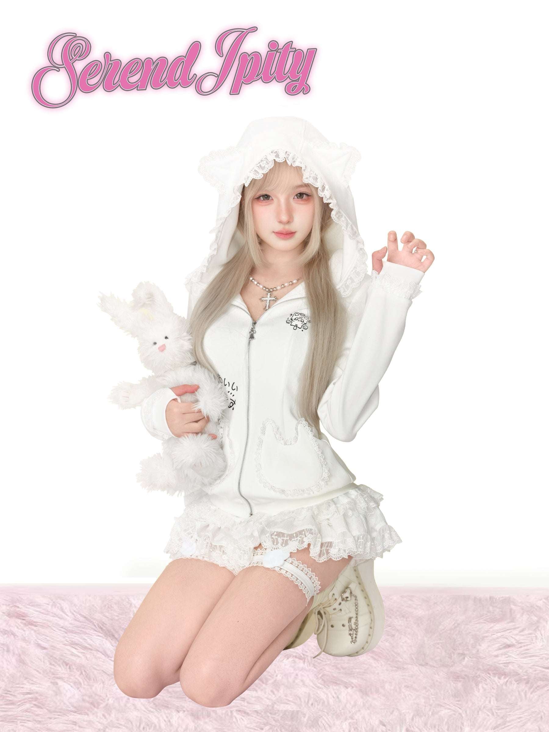 Person wearing a white outfit with a hood, holding a plush toy, on a pink fluffy surface