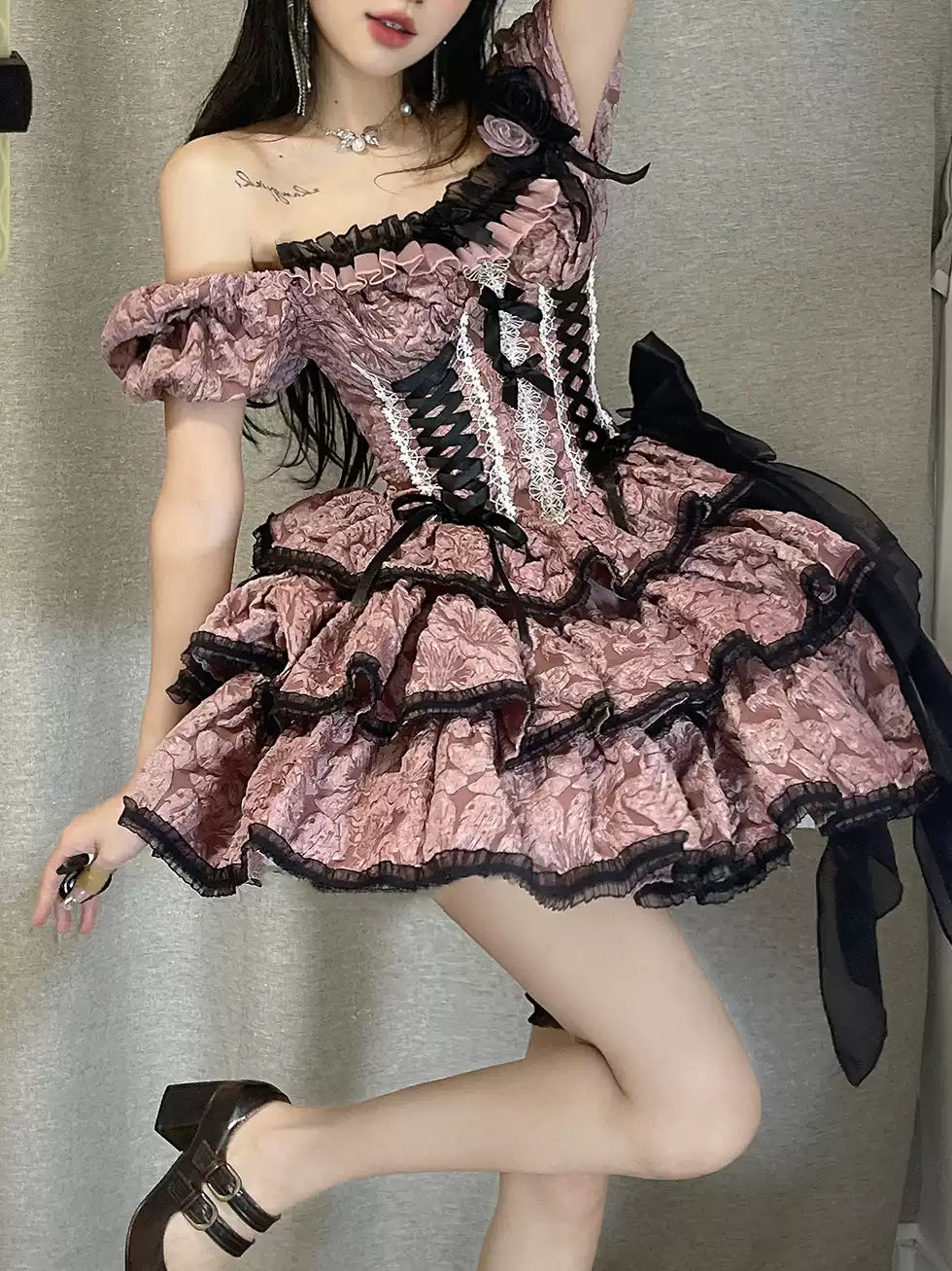 Person wearing a pink and black lace dress with ruffles against a neutral background