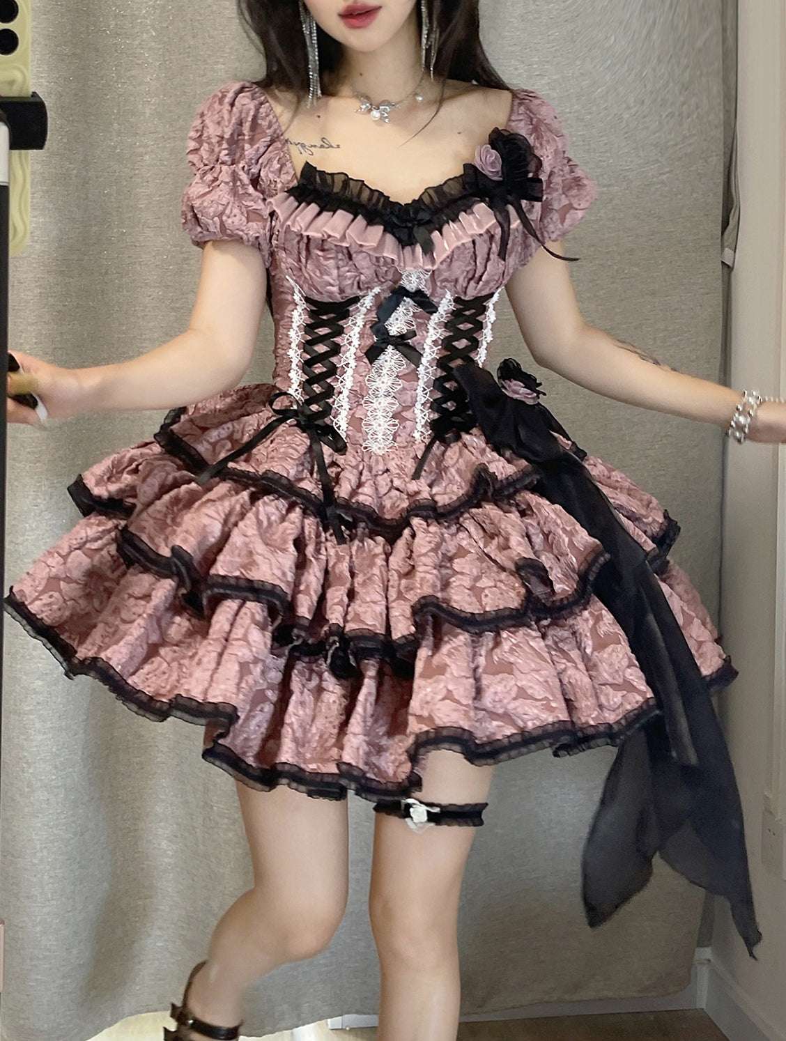 Person wearing a pink and black ruffled dress with a plain background