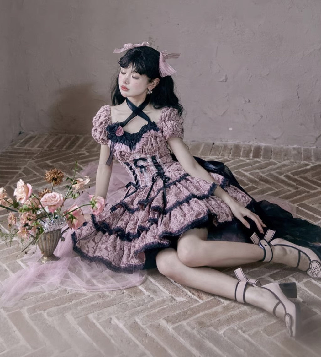 Woman in a pink and black dress sitting on a stone floor with flowers.