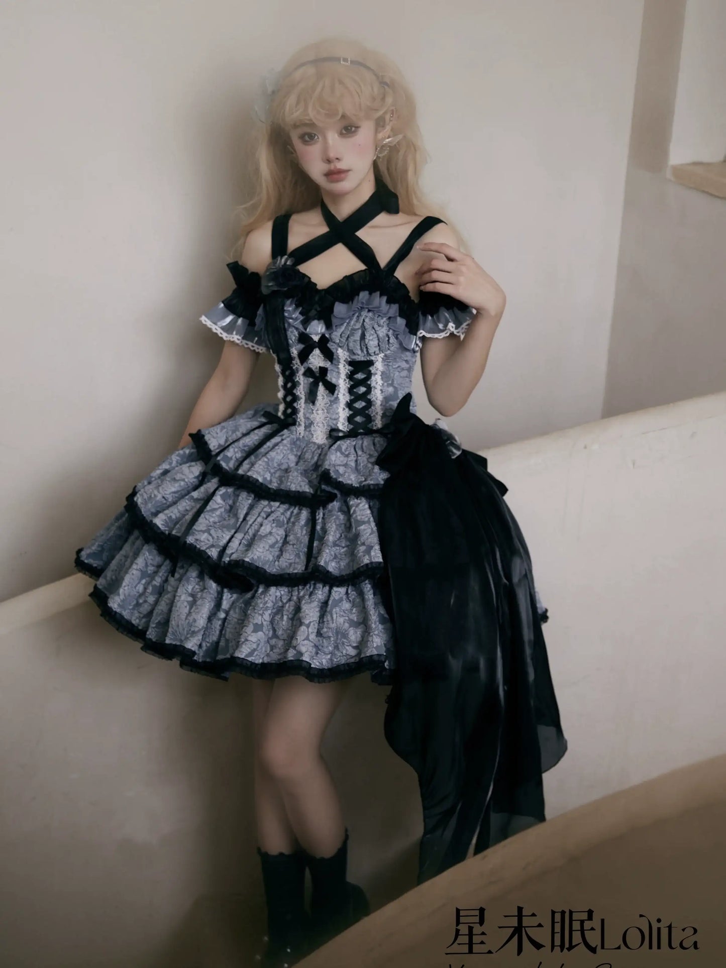 Person wearing a black and gray dress with ruffled details, sitting on a white surface.