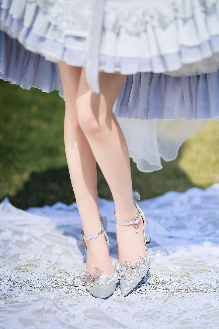 Person wearing a light blue dress with ruffles and silver high heels on a blurred natural background